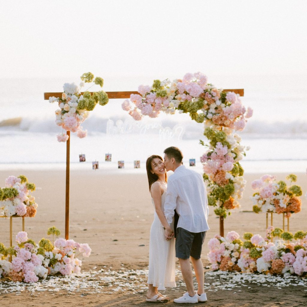 Happy bride and groom celebrating their sunset proposal at Melasti Beach with pink decorations.