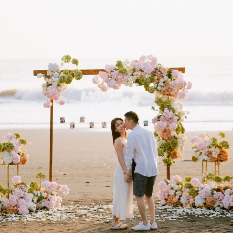 Happy bride and groom celebrating their sunset proposal at Melasti Beach with pink decorations.